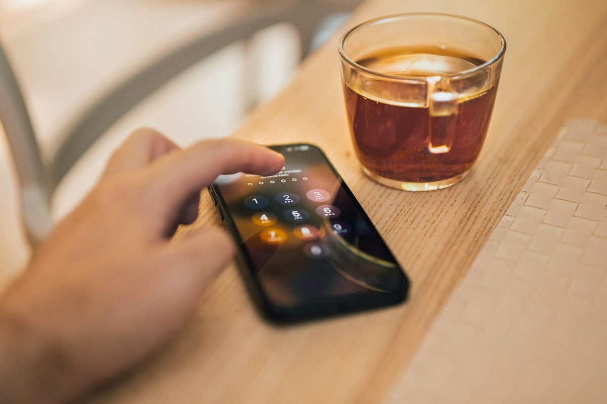 Person med mobiltelefon og kaffekopp ved bordet