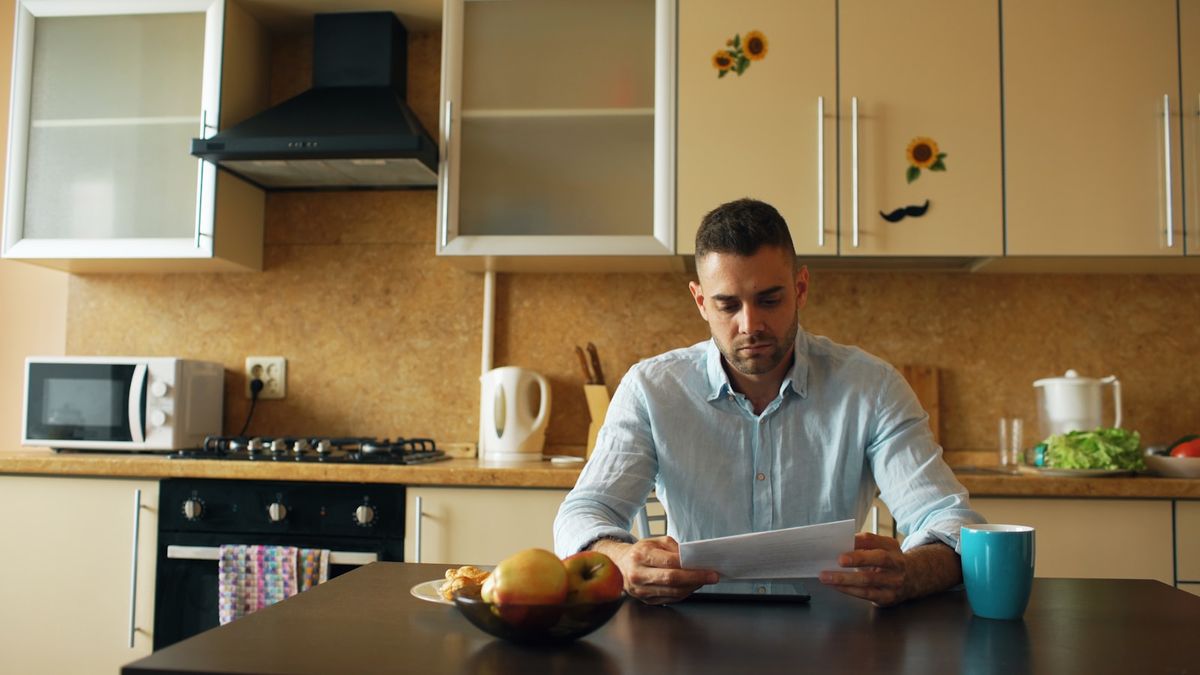 Mann leser dokumenter ved kjøkkenbordet med kaffe om morgenen