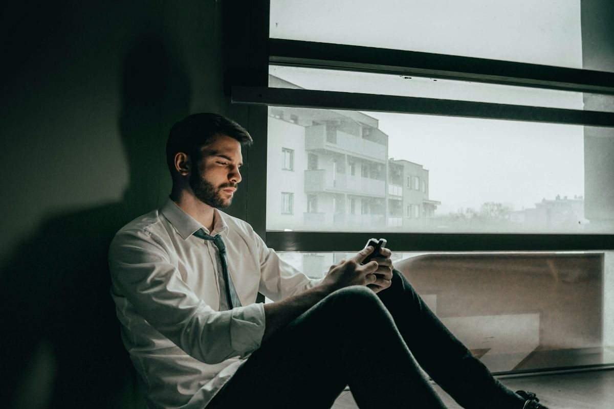 Bekymret person ser på mobilen ved vinduet